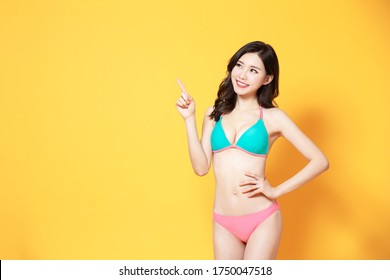 asian woman with bikini swimsuit and point to copyspace isolated yellow background