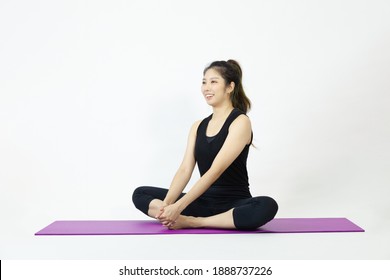 Asian Woman In Black Sportswear Sitting On Purple Yoga Mat Pose On The White Background.