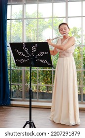 Asian Woman Blowing The Flute, A Universal Classical Instrument. The Concept Of A Classical Music School. Music Teacher