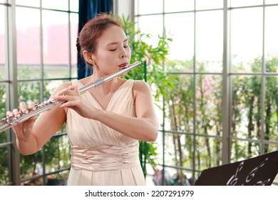 Asian Woman Blowing The Flute, A Universal Classical Instrument. The Concept Of A Classical Music School. Music Teacher