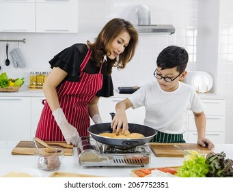 Asian woman and boy putting fresh buns on hot pan while cooking burgers for lunch in kitchen at home. Conept for love and relationship time shairing in modern family.