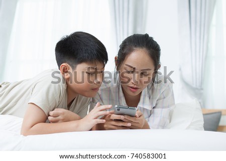 Asian woman with asian boy watching smartphone on bed.