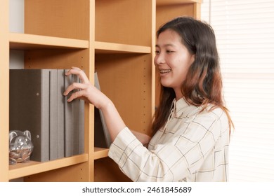 Asian woman with braces placing file on wooden bookshelf in professional office setting. Scene portrays organized, focused, and diligent work environment with emphasis on neatness. - Powered by Shutterstock