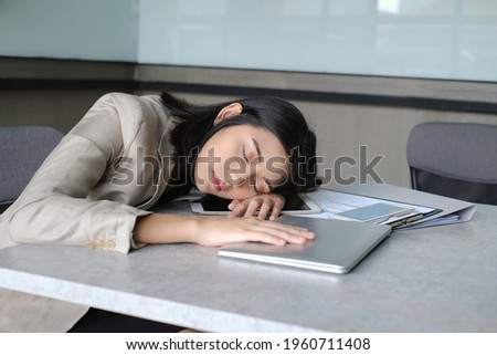 An asian woman in brown suit fall asleep at her desk with closed labtop, smartphone and her work things in office. resting a while in office.