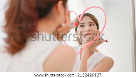 asian woman with brunette ponytail draws a heart shape use lipstick on the mirror and look at herself feeling confident self love