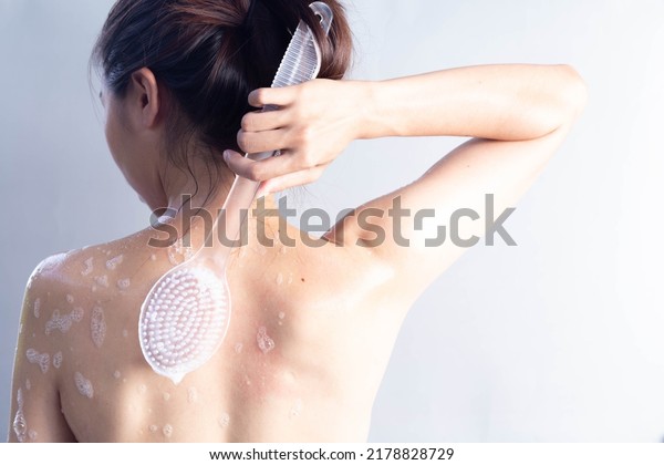 Asian woman brushing her back, shower scrubbing back\
view, cleaning back skin