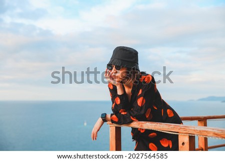 Asian woman in bucket hat and sunglasses enjoying ocean view from balcony