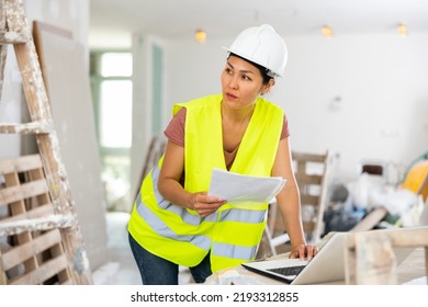 Asian Woman Builder Checking Project Documentation And Using Laptop While Working In Apartment.