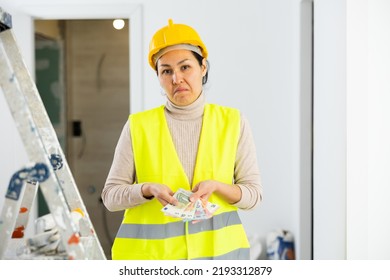 Asian Woman Builder In Hardhat And Yellow Vest, Holding Bunch Of Cash, Frustrated By Her Salary.