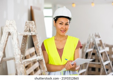 Asian Woman Builder Holding Documents, Smiling And Looking At Camera. Repair Works In House.