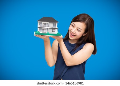 Asian Woman Builder Holding Home Model Isolated On Blue Background, Real Estate House And Renovated Property Concept