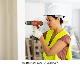 Asian Woman Builder Using Drill To Bore Hole In Wall During Repair Works In Apartment.