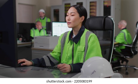 Asian Woman Builder Working On Computer In Office. Female Engineer Wearing Uniform In Office Uses Computer 