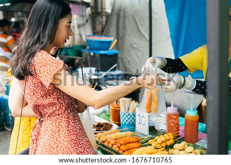 Asian woman buying fried hotdog on a stick - Street food in Thailand.