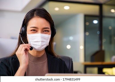 Asian Woman Call Center With Face Mask For Hygiene In The Office And Another Employee Using Heandphone Speaker.Speaking Assistant Office.Thai Face.