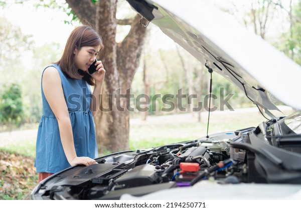 Asian woman calling garage after car breaks\
down. woman opening car hood and call to insurance or someone to\
help after the car breaks down, park on the side of the road.\
Transportation concept.