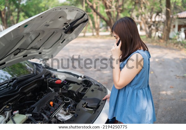 Asian woman calling garage after car breaks
down. woman opening car hood and call to insurance or someone to
help after the car breaks down, park on the side of the road.
Transportation concept.