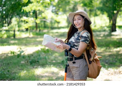 An Asian Woman In Camaflag T-shirt And Brown Short Bag Packing, Holding Map, Stamding In Fresh Green Wood Smiling To Camera. Walking, Claimbing Mountain Concept.