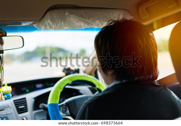 Asian woman\
carefully drive a sedan on the highway. The inside view of the car\
show the car dashboard, steering wheel and the rear window. The sun\
set shining on the driver\'s\
hair.