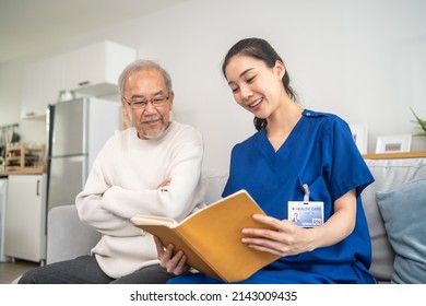 Asian Woman Caregiver Take Care Of Senior Elderly Male At Nursing Home. Young Female Therapist Doctor Sit On Sofa, Reading A Book To Happy Older Mature Man Patient. Medical Insurance Service Concept