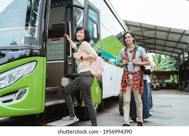 Asian woman carrying a backpack and headphones while holding the door handle gets into the bus with the background of passengers lining up to get on the bus - Shutterstock ID 1956994390