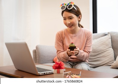 Asian Woman Celebrating Birthday Through Video Call Online Virtual Party At Home While Isolated Stay At Home. Hand Holding Cup Cake