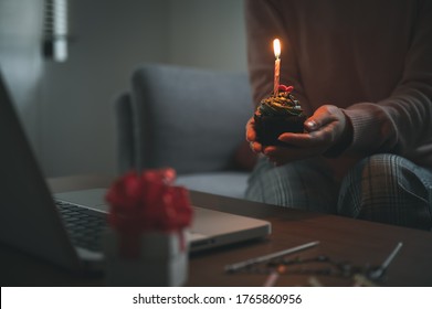 Asian Woman Celebrating Birthday Through Video Call Online Virtual Party At Home While Isolated Stay At Home. Hand Holding Cup Cake Light Up Candle