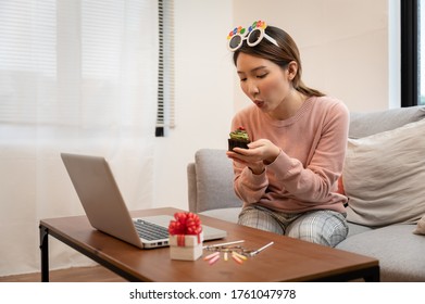 Asian Woman Celebrating Colleague Birthday Through Video Call Online Virtual Party At Home While Isolated Stay At Home. Hand Holding Cup Cake