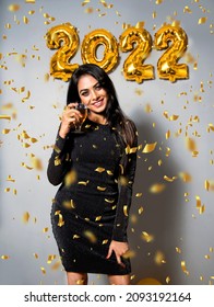  Asian Woman Celebrating At Party. Portrait Of Beautiful Girl Holding Champagne Glass In Hand Wearing Shine Black Dress Having Fun With Golden 2022 Balloons, Confetti. New Year 2022 Concept.