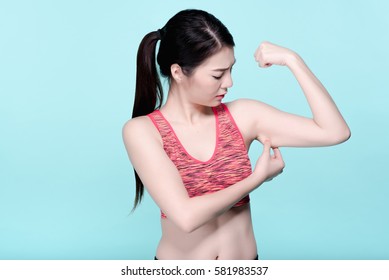 Asian Woman Checking Arm Cellulite After Workout. Beauty Face And Natural Makeup Sports Bra Outfit. Isolated Over Blue Background