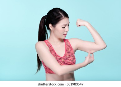 Asian Woman Checking Arm Cellulite After Workout. Beauty Face And Natural Makeup Sports Bra Outfit. Isolated Over Blue Background