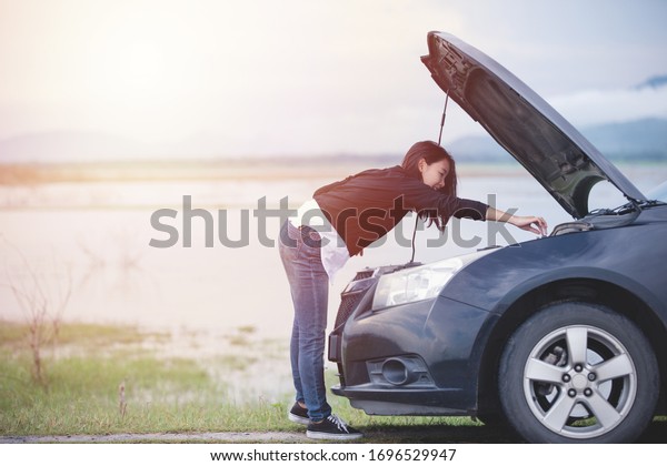 Asian woman\
checking broken down car on\
street
