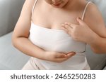 Asian woman checking lumps on her breast for signs of breast cancer by her self at home. Healthcare and medical concept.