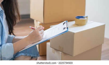 Asian woman checking and packing the carton box prepare to move to new house relocation shipping or check goods package before delivery to customer from online shopping by checklist - Shutterstock ID 2225734503