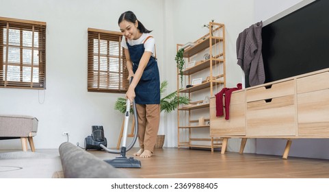 Asian woman cleaning in living room at home. Housekeeper or maid cleaner feel happy use vacuum cleaner to clean - Shutterstock ID 2369988405