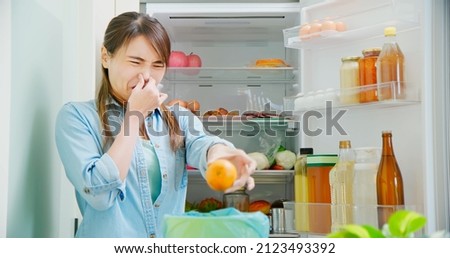 asian woman is cleaning refrigerator and pouring food waste which smell bad into kitchen bucket at home