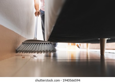 Asian woman cleaning and sweeping dust the floor under the sofa with a broom in the living room. Woman doing chores at home. Housekeeping concept. - Powered by Shutterstock