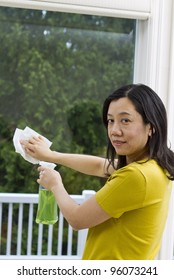 Asian Woman Cleaning Window With Spray Bottle And Paper Towel In Hand