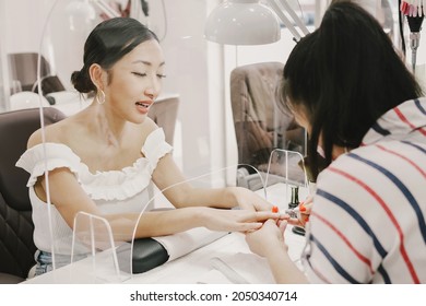 Asian Woman Client Getting A Manicure In Nail Salon, With Protective Screen, Social Distancing Covid-19 Pandemic Procedure, Reopenning Small Business, Health And Beauty Lifestyle Concept