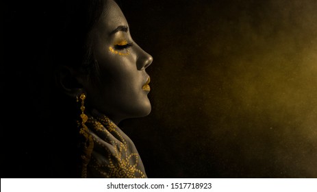 Asian Woman, Close-up Face Black Skin And Painting Gold And Spray Gold Powder In Dark Background.