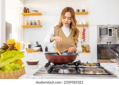 Asian woman cooking healthy food fried pasta in cooking pan on modern kitchen island stove at home. Attractive girl preparing food for dinner party celebration meeting with friend on holiday vacation. - Powered by Shutterstock