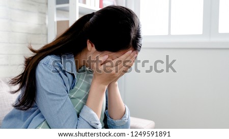 asian woman in cozy room sitting in sofa using hands cover face disappointed crying. emotional girl lovelorn tears heart pain concept staying home feeling broken. unhappy lady sadness indoors.