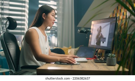 Asian woman creating 3D model of video game character in professional program using computer and digital tablet while working at home office
