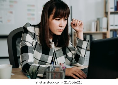 Asian Woman Creative Worker Having Blurred Vision Is Squinting Eyes While Leaning Forward Close To The Computer Monitor Trying To See Clearly At Office Desk.