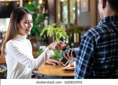 Asiatische Kundin mit Kreditkarte Schnaps auf Kreditkartenleser EDC-Maschine, um einen Kellner für den Kaffeekauf am Tisch in Café zu bezahlen.