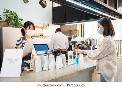 Asian Woman Customer Wear Mask Due To Covid-19, Order Drink To Waitress On Coffee Bar Counter. Young Girl Use Sanitizer Gel To Clean And Wash Hand Before Receive Takeaway Food From Restaurant Worker