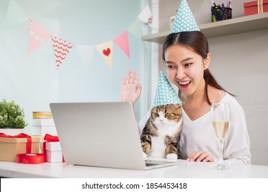 Asian Woman And Cute Cat Enjoy Celebrating And Waving In Party Via Video Call Conference With Friends And Family, New Normal For Birthday Christmas And New Year Party.