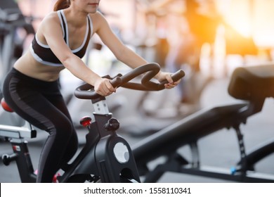 Asian Woman Cycling On Bike In Fitness Gym.