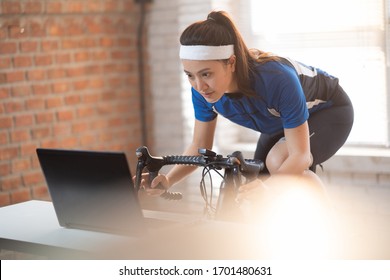 Asian Woman Cyclist. She Is Exercising In Home.by Cycling On The Trainer And Play Online Bike Games