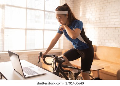 Asian Woman Cyclist. She Is Exercising In Home. By Cycling On The Trainer.she Is Wiping Sweat